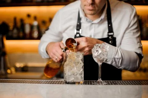 Barman adding alcoholic drink into a glass filled with ice cubes Foto stock