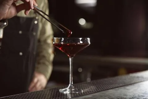 Barman adding cherry into cosmopolitan martini cocktail at counter, closeup.  Stock Photos