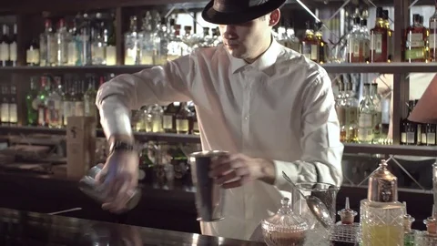 Barman in a black hat and white shirt prepares a cocktail using a shaker, jiger Stock Footage 77530452