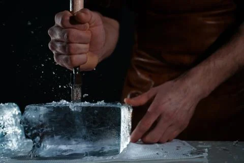 Barman chopping ice using a special knife. Сhunks of ice flying around Stock Photos
