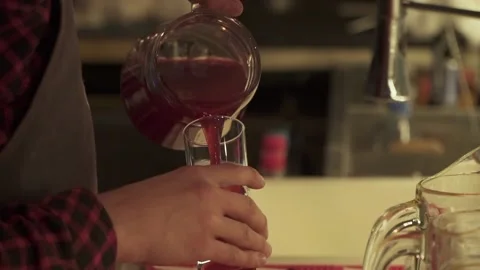 Barman pours fruit drink from jug into a glass. Red homemade wine in a decanter Stock Footage 133354077