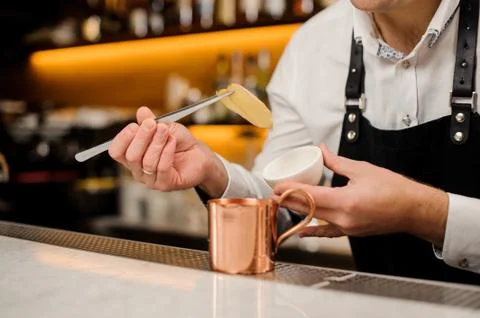 Barman in white shirt adding two slices of ginger into a cup Foto stock