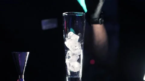 A barman's hand putting ice cubes into a transparent a long glass in dark Stock Footage 141109810