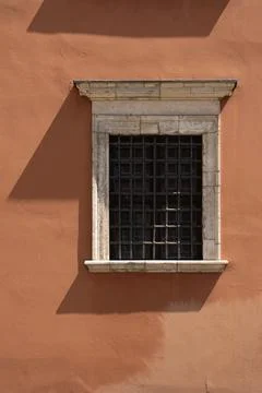 Barred window with stone frame on orange historic building wall Stock Photos