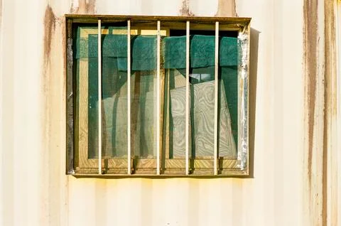 Barred Window on a Weathered Wall With Blue Curtain Foto stock