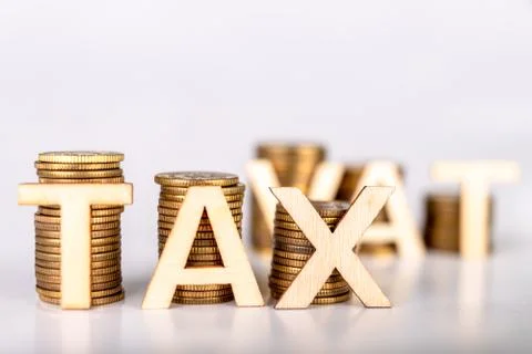 Bars stacked from coins on a white table. TAX and VAT lettering with wooden l 库存照片