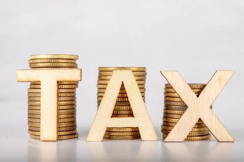 Bars stacked from coins on a white table. TAX lettering with wooden letters b Stock Photos