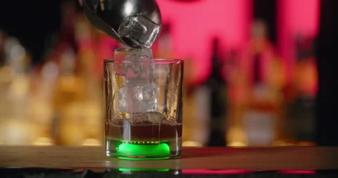 Bartender adds ice cubes to the glass with green backlight in slow motion Video stock 156070254