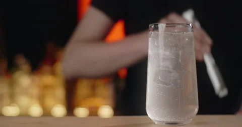 Bartender adds ice cubes to the glass with refreshment beverage in slow motion Stock Footage 157456201