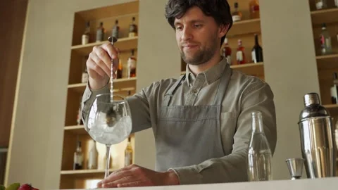 Bartender in the apron stirring an ice cubes in the cocktail glass on the Stock-Footage 153458695