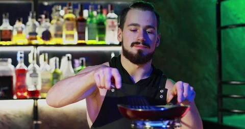 The bartender with a beard prepares a delicious cocktail on a round gas burner. Stock Footage 103385399