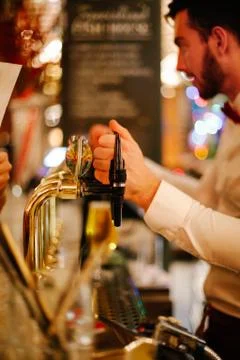 Bartender behind the counter taking an order in a pub, hands on taps. Stock Photos