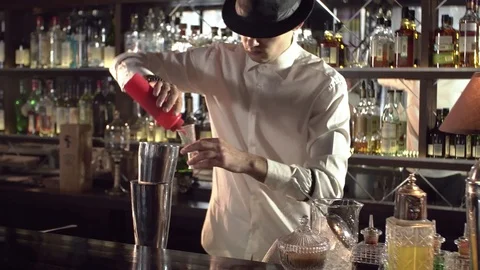 Bartender in a black hat and white shirt prepares a cocktail while standing Stock Footage 77529987