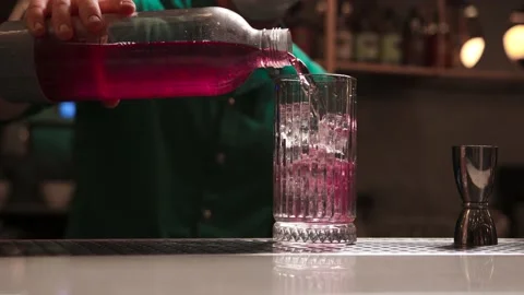 The bartender from a bottle pours pink gin into a faceted glass with ice Stock Footage 164558915