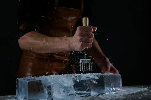 Bartender chopping ice using a special knife. Сhunks of ice flying around Stock Photos