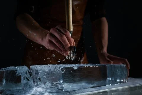 Bartender chopping ice using a special knife. Peaces of ice goes around Stock Photos