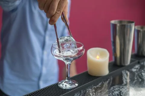 Bartender cools the glass with ice before making a cocktail. Close up photo Stock Photos