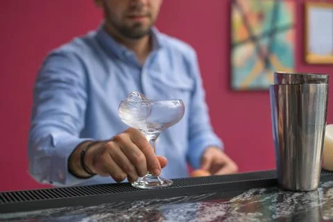 Bartender cools the glass with ice before making a cocktail. Close up photo Stock Photos