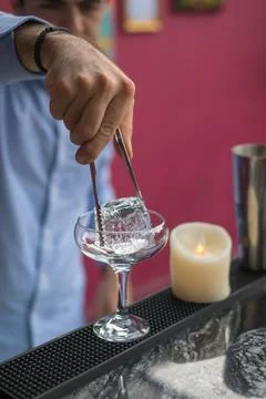 Bartender cools the glass with ice before making a cocktail. Close up photo Stock Photos