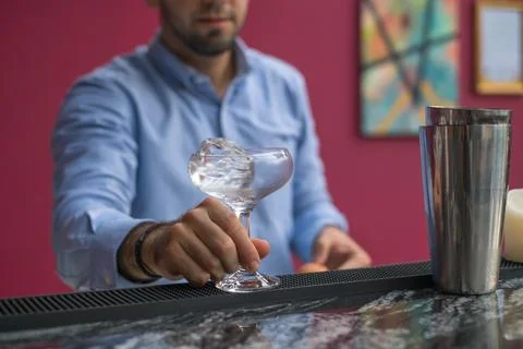 Bartender cools the glass with ice before making a cocktail. Close up photo Stock Photos