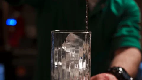 Bartender at the counter is stirring ice in a cocktail glass with a metal spoon Stock Footage 164559167