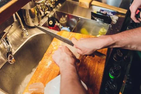 Bartender is cutting a large block of ice to prepare whiskey cocktails Stock Photos