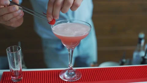 Bartender decorates a finished alcoholic cocktail with a cherry. Close-up of a Stock Footage 322731590