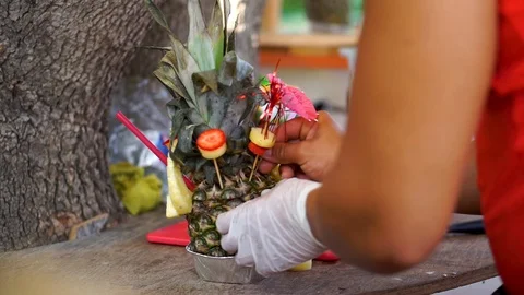 Bartender Decorating Tropical Pineapple Cocktail on Beach and Giving to Customer Stockbeeldmateriaal 129185945