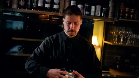 Bartender in dimly lit bar preparing a cocktail with a stainless shaker Stock Footage 318654935
