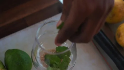 Bartender dropping mint leaves into passion fruit mojito cocktail glass Stock Footage 230080376