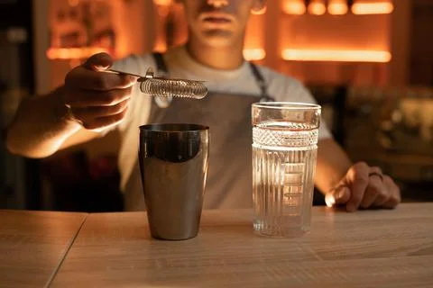 Bartender filtering cocktail through sieve into glass pours alcoholic beverag Stock Photos