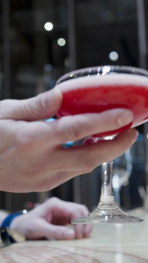 Bartender Hand Holding a Vibrant Red Cocktail in a Coupe Glass at a Bar. Cl.. Stock Footage 333915113