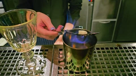 Bartender handles a slotted absinthe spoon over a metal cup as blue flames Vidéo 340213198