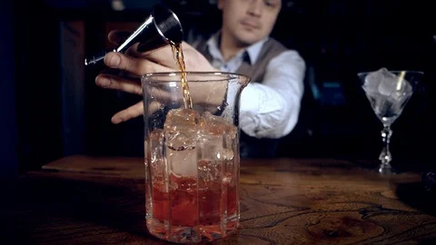 The bartender makes a cocktail by pouring whiskey or tequila from a jigger. Stock Footage 124373300