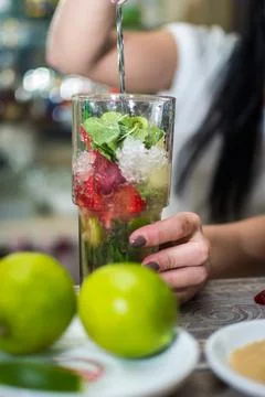 Bartender making refreshing coctail on a bar background. Dark moody style. Ic Stock Photos