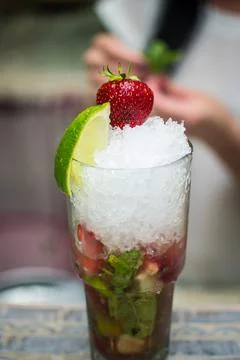 Bartender making refreshing coctail on a bar background. Dark moody style. Ic Stock Photos
