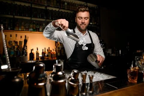 Bartender masterfully pours ice cubes from scoop into a shaker cup 스톡 사진