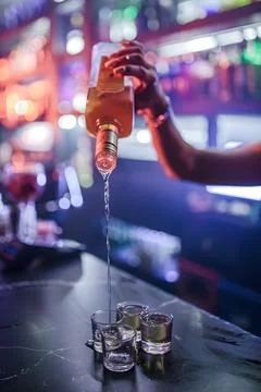 Bartender pouring alcoholic drink into shot glasses 写真素材