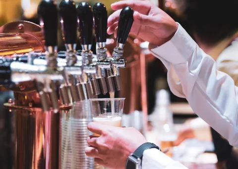 Bartender pouring draft beer in the bar, Barman hand at beer tap pouring drau Stock Photos