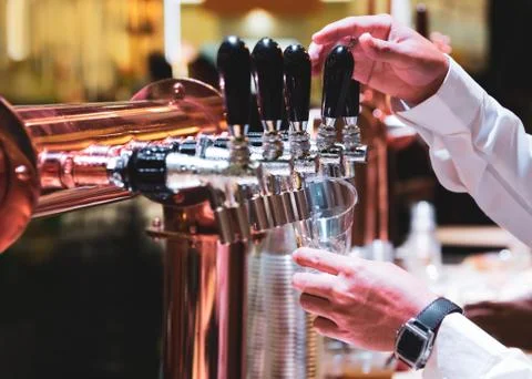 Bartender pouring draft beer in the bar, Barman hand at beer tap pouring drau Stock Photos