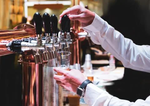 Bartender pouring draft beer in the bar, Barman hand at beer tap pouring drau Stock Photos