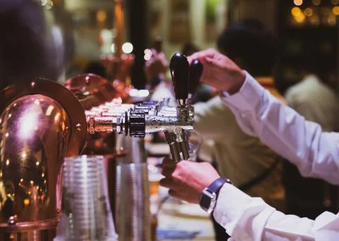 Bartender pouring draft beer in the bar, Barman hand at beer tap pouring drau Stock Photos
