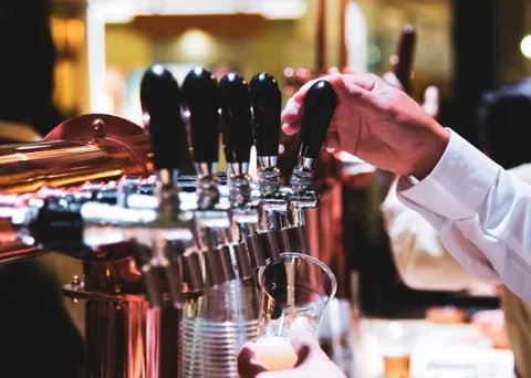 Bartender pouring draft beer in the bar, Barman hand at beer tap pouring drau Stock Photos