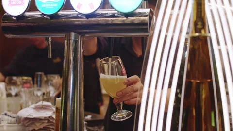 Bartender Pouring Draft Beer Into Glass at Bar Counter in Busy Nightlife Setting 스톡 동영상 342287213