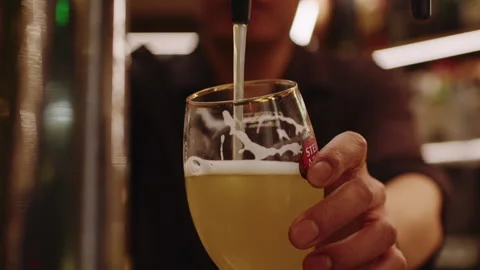 Bartender Pouring Draft Beer Into Glass at Bar Counter in Warm Indoor Setting 스톡 동영상 342469063