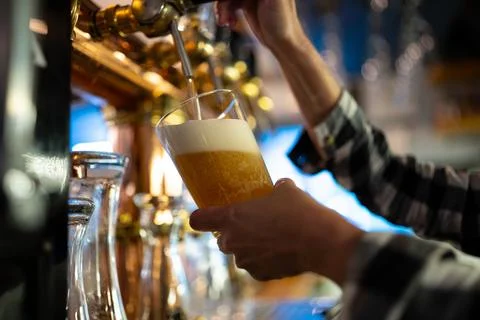 Bartender pouring fresh draft beer into glass from tap at bar with soft lighting Stock Photos