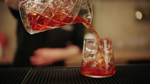 Bartender pouring a freshly mixed red cocktail into a glass filled with ice Stock Footage 332665536