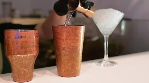 Bartender pouring liquid into a copper cocktail shaker using a jigger, with a Stock Footage 293521401