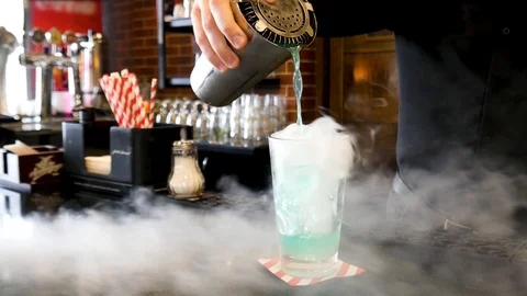 Bartender pouring liquid from shaker to a cocktail glass with white cold smoke Stock Footage 116330860