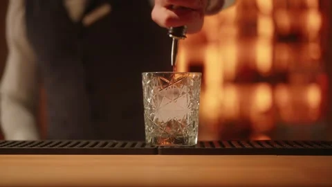 Bartender pouring red bitter cocktail into crystal glass with ice cube. Stock Footage 337404790